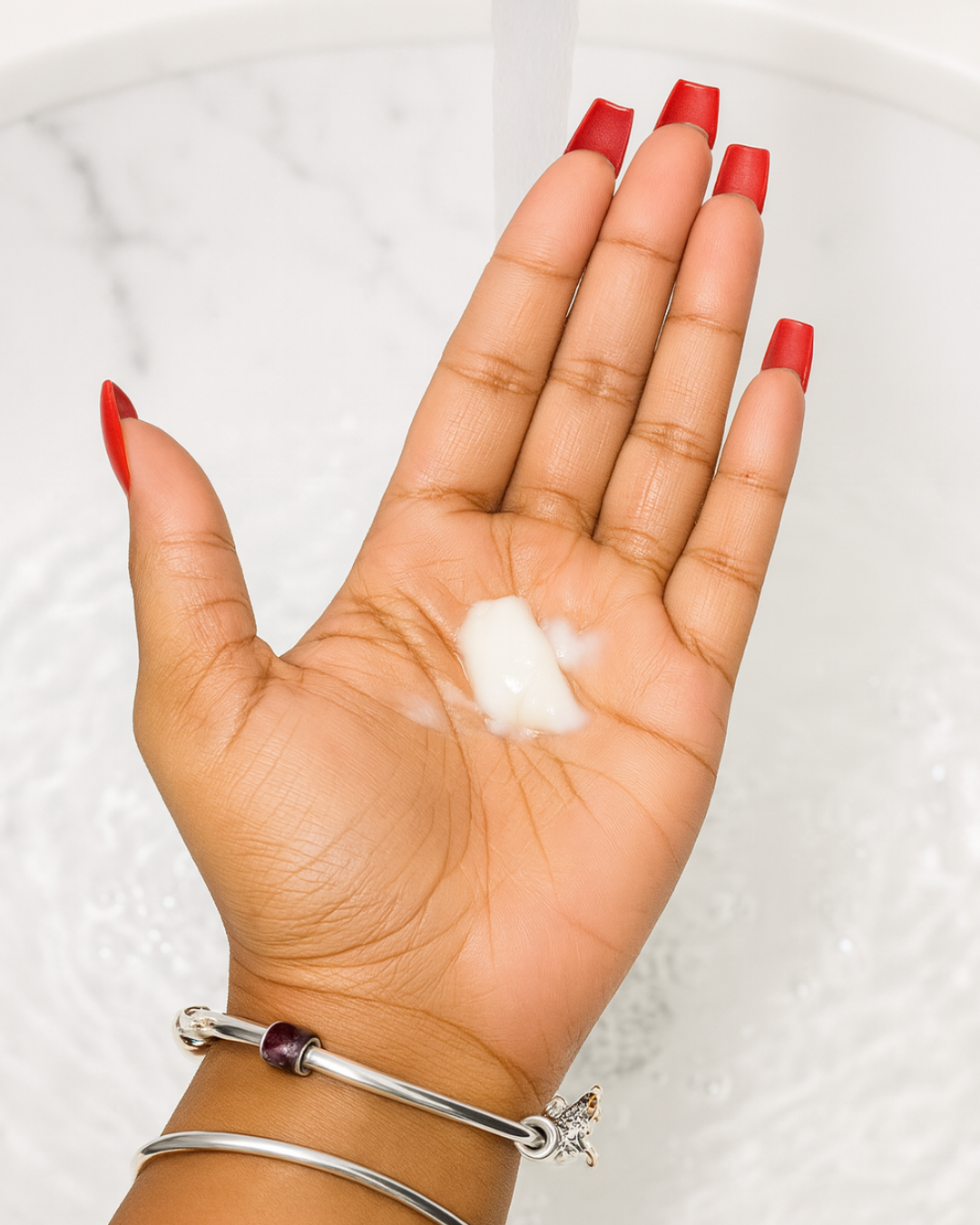 Hand with red nail polish holding a small amount of radiance replenish face wash against a light background